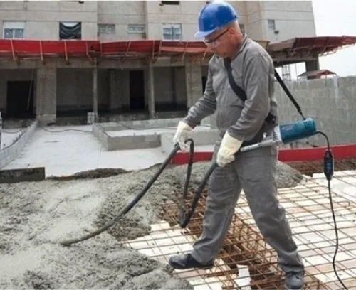 Vibrador portátil para concreto em uso: operário de capacete adensando o concreto fresco de uma laje (foto ilustrativa, não é da empresa)
